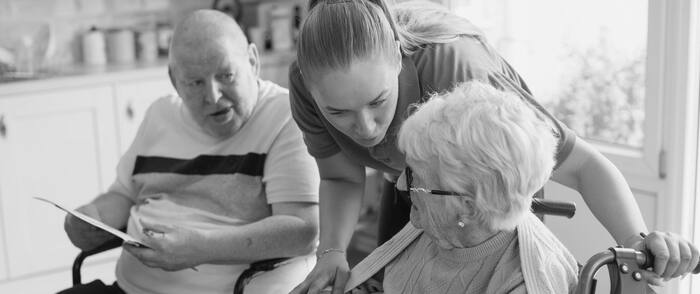 Pflegefachperson im Gespräch mit zwei Patienten im Rollstuhl
